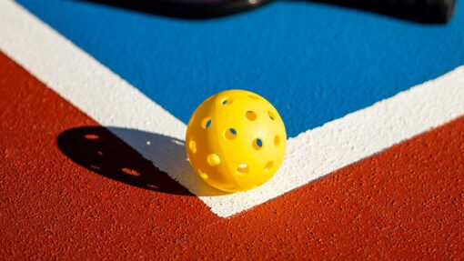 Yellow perforated plastic ball resting on a red running track with blue and white lines nearby.